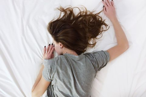 Ein Mädchen liegt mit Haaren vor dem Gesicht auf dem Bett.
