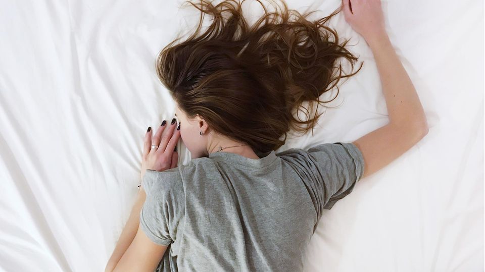 Ein Mädchen liegt mit Haaren vor dem Gesicht auf dem Bett.