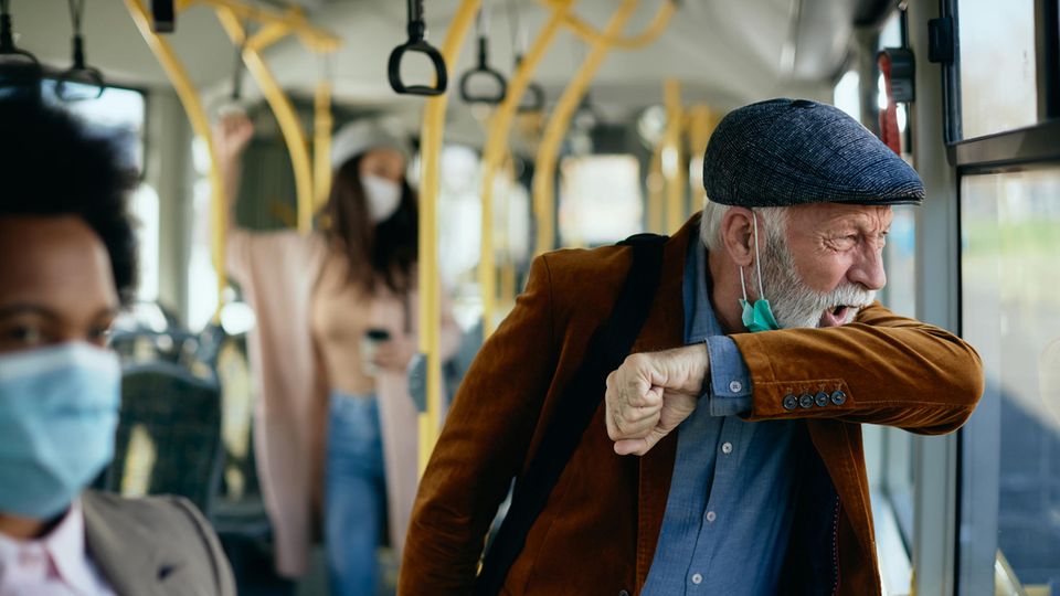 Ein älterer Herr hustet in einem Bus
