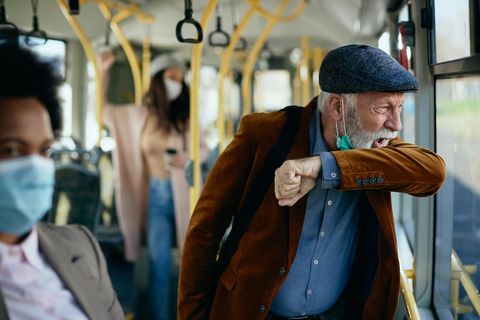 Ein älterer Herr hustet in einem Bus