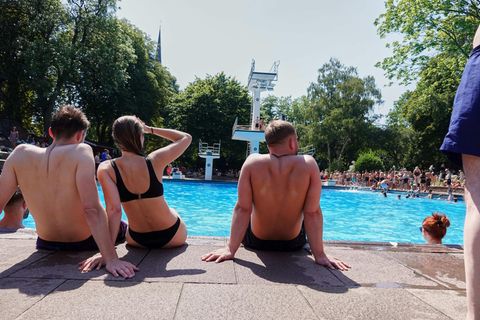 Sommer 2022: Badegäste sitzen bei strahlendem Sonnenschein und hohen Temperaturen im Hamburger Kaifu-Freibad