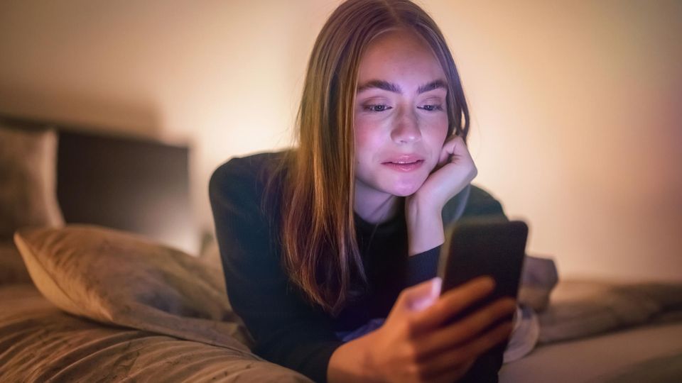 Mujer joven acostada en la cama mirando su teléfono inteligente