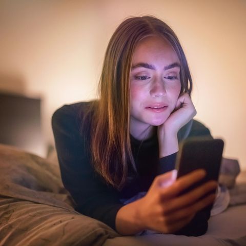 Eine junge Frau liegt im Bett und schaut ihr Smartphone