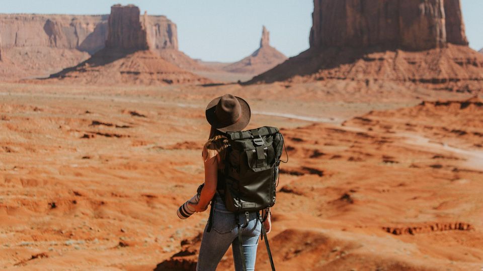 Eine Frau mit Hut steht vor einer Wüstenlandschaft.