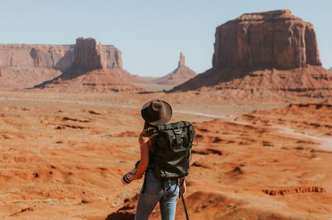 Eine Frau mit Hut steht vor einer Wüstenlandschaft.