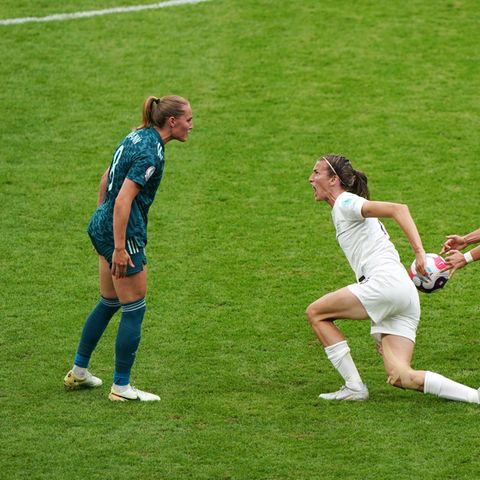 Eine weiße Fußballspielerin ganz in Weiß springt mit weit aufgerissenem Mund auf und nähert sich ihrer Gegenspielerin in Grün