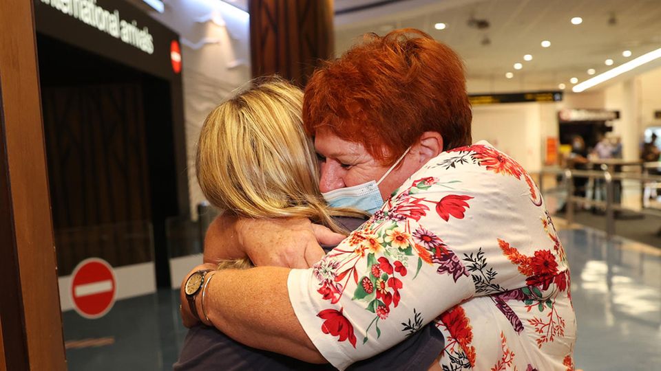 Zwei weiße Frauen umarmen sich innig in einem Flughafen-Terminal