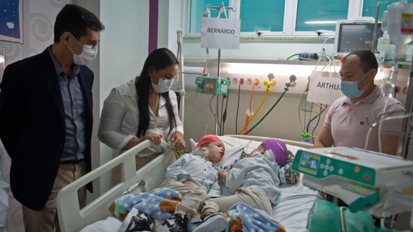 Nach der OP stehen die Eltern der Zwillinge am Krankenbett ihrer Kinder