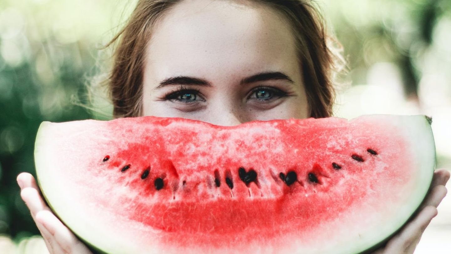 Eine Frau grinst mit einer Wassermelone vor dem Mund in die Kamera. Eine Frau grinst mit einer Wassermelone vor dem Mund in die Kamera.