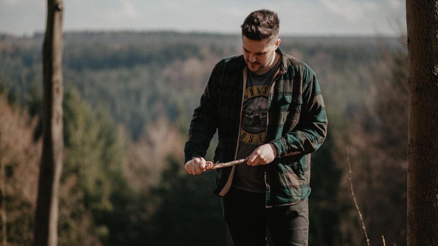 Ein Mann schnitzt im Wald einen Stock.