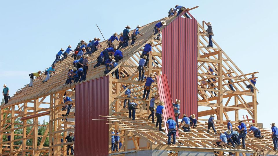 Männer im Blaumann bauen ein neues Holzhaus.