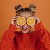 Eine Frau hält sich grinsend zwei Orangenhälften vor die Augen.