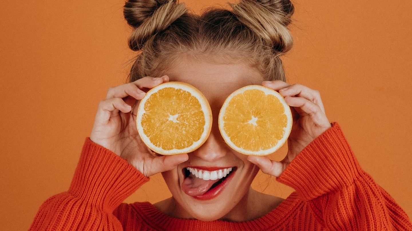 Eine Frau hält sich grinsend zwei Orangenhälften vor die Augen.