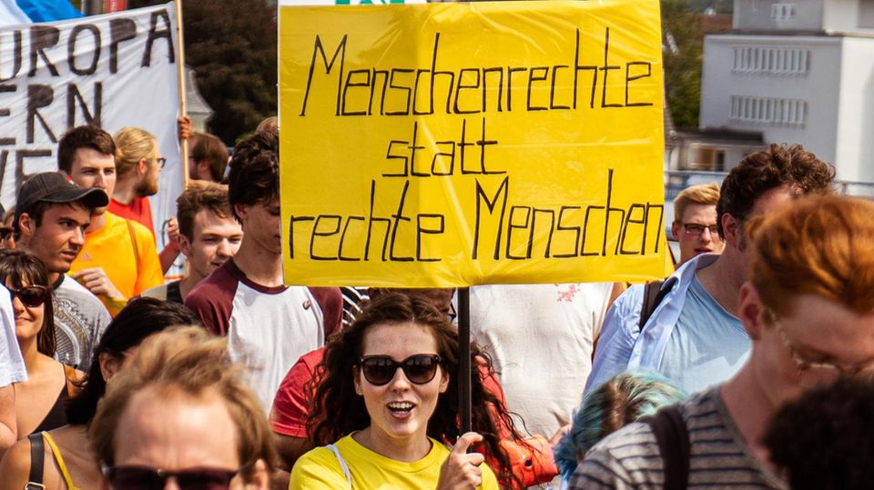 Eine Frau hält ein Protestschild mit der Aufschrift "Menschenrechte statt rechte Menschen" hoch.