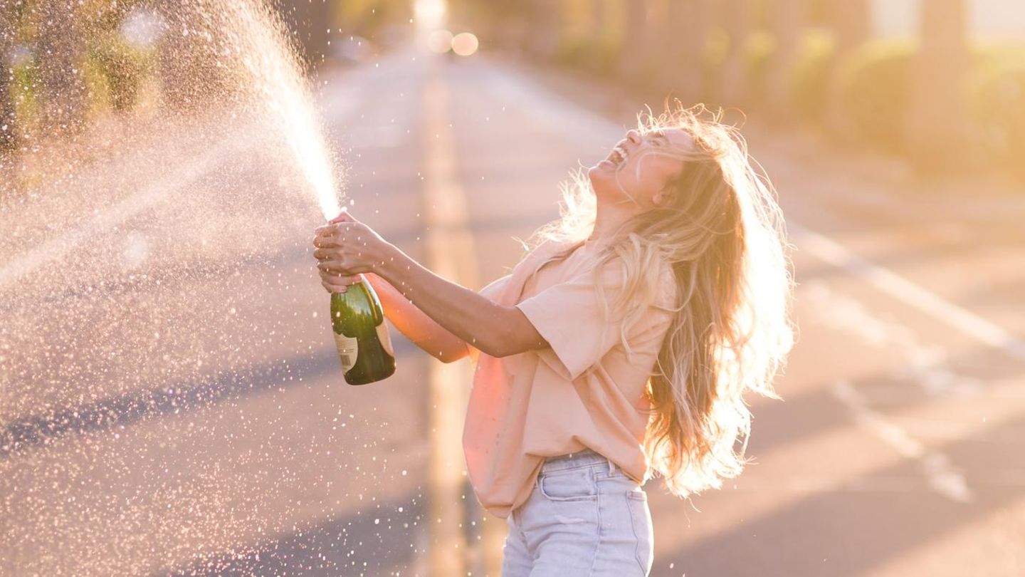 Eine Frau öffnet lachend eine Sektflasche.