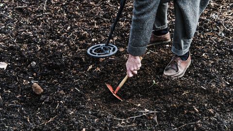 Mann gräbt mit Metalldetektor gräbt mit einer Hacke im Boden