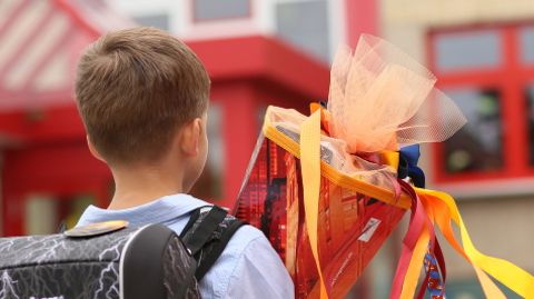 Ein Junge steht mit einer Schultüte in der Hand vor einem Schulgebäude