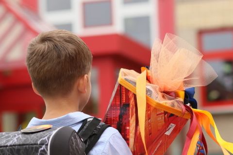 Ein Junge steht mit einer Schultüte in der Hand vor einem Schulgebäude