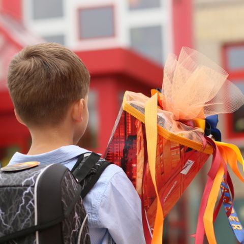 Ein Junge steht mit einer Schultüte in der Hand vor einem Schulgebäude