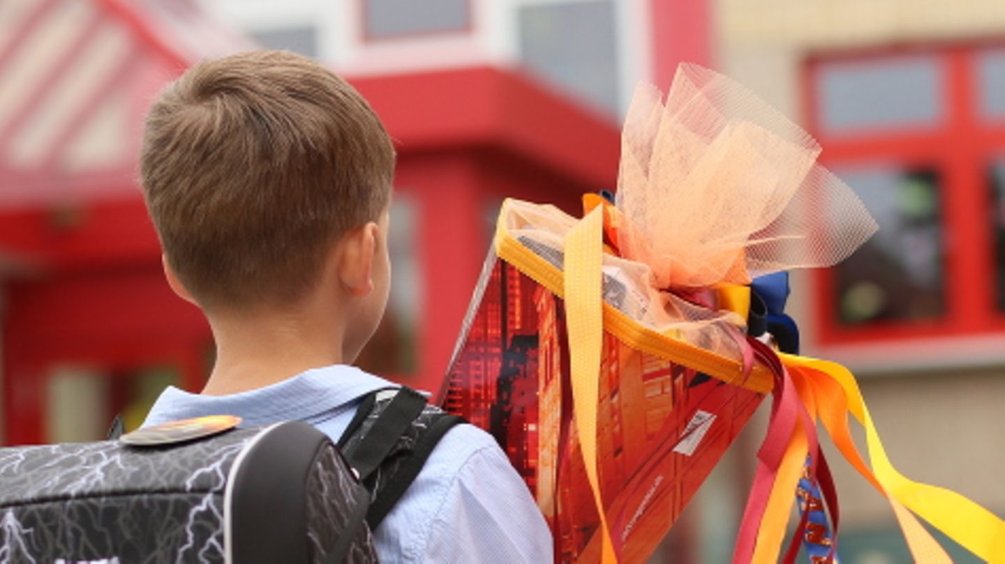 Ein Junge steht mit einer Schultüte in der Hand vor einem Schulgebäude