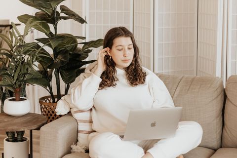 Eine Frau sitzt mit dem Laptop auf dem Sofa.
