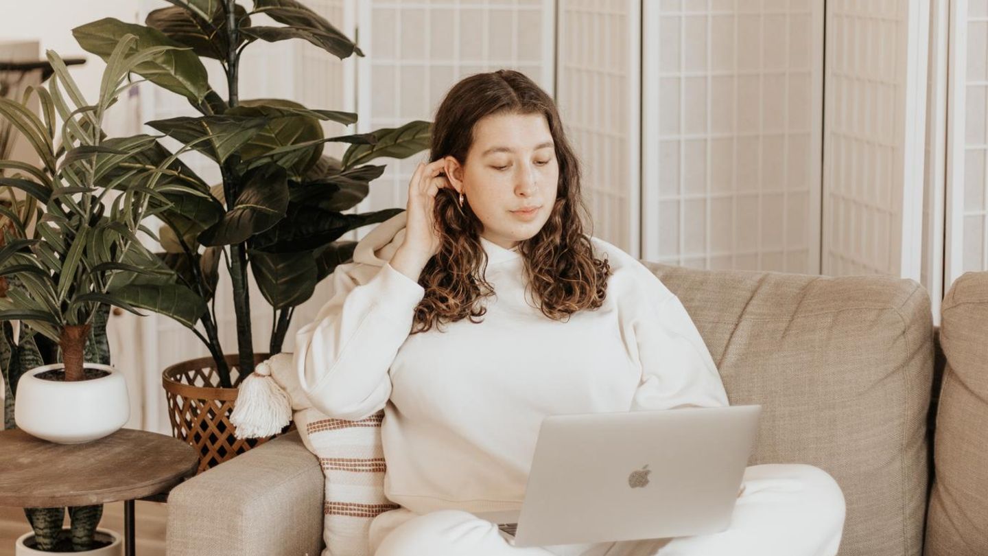 Eine Frau sitzt mit dem Laptop auf dem Sofa.