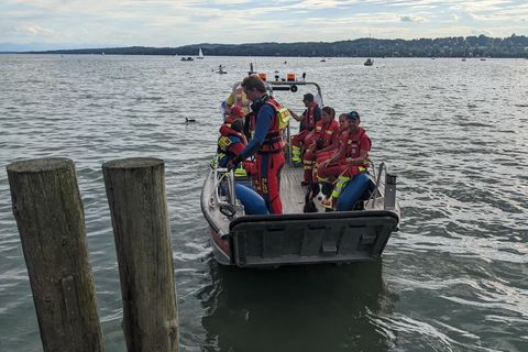 Auf einem großen See fährt ein Aluminium-Boot voller Menschen in der roten Kleidung der Wasserwacht