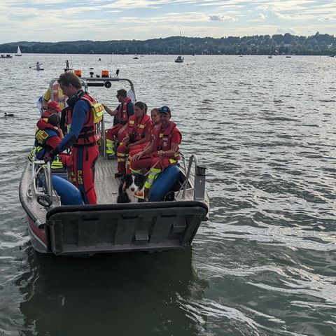 Auf einem großen See fährt ein Aluminium-Boot voller Menschen in der roten Kleidung der Wasserwacht