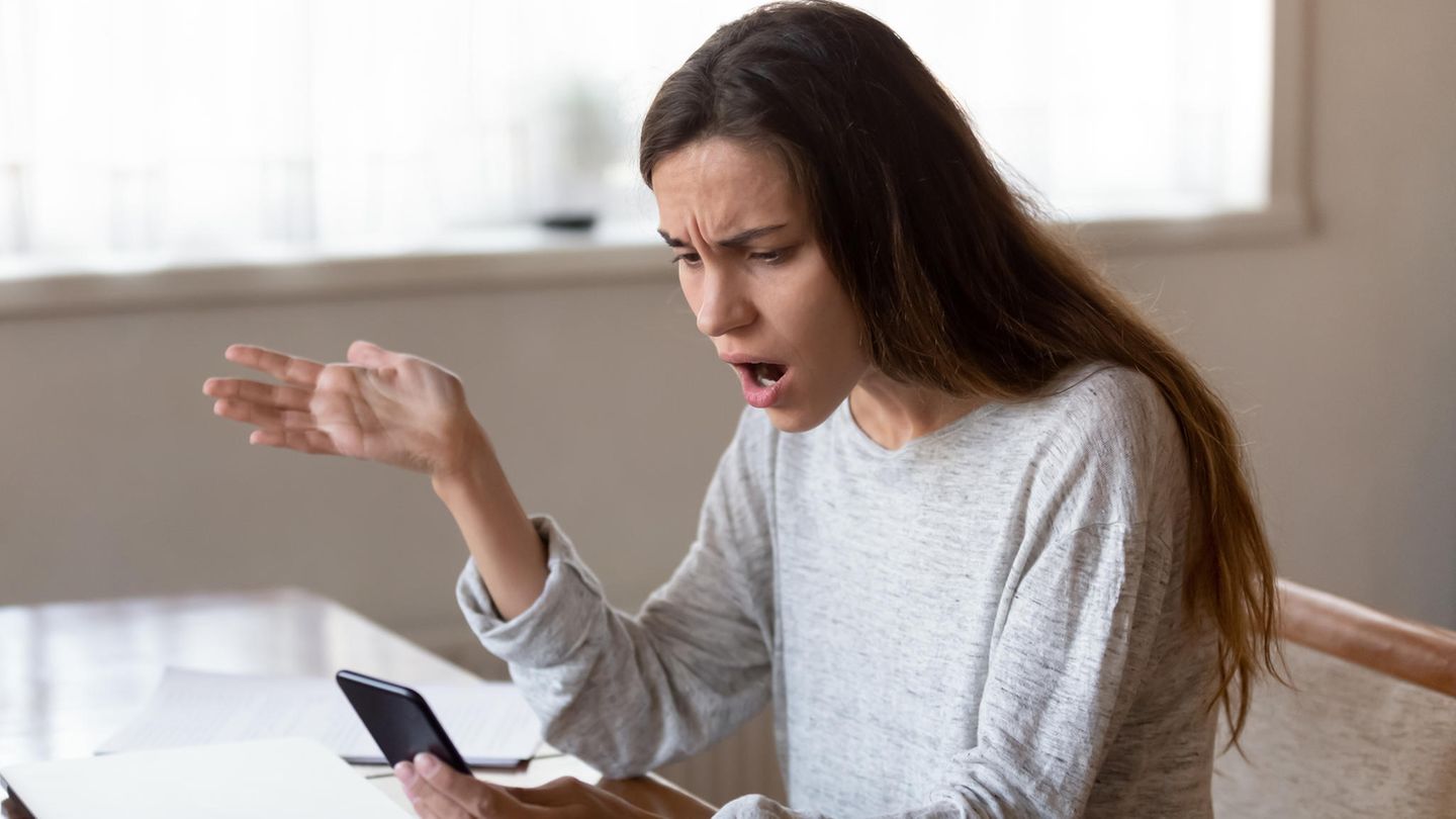 Eine junge Frau starrt geschockt auf ihr Smartphone