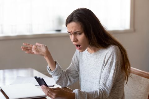 Eine junge Frau starrt geschockt auf ihr Smartphone