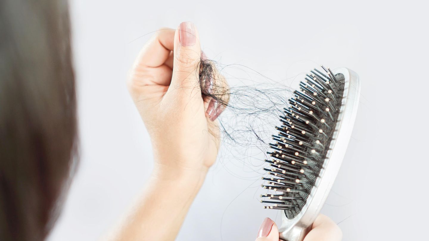 Frau zieht viele Haare aus der Bürste und hat Haarausfall