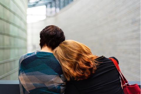 Eine Frau steht angelehnt an einen Mann vor einem Haus.