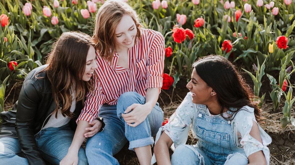 Drei Frauen sitzen lachend vor einem Tulpenfeld.