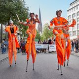 Orange gekleidete Teilnehmer laufen bei der Parade zum Christopher Street Day (CSD) auf Stelzen über die Mönckebergstraße