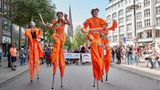 Orange gekleidete Teilnehmer laufen bei der Parade zum Christopher Street Day (CSD) auf Stelzen über die Mönckebergstraße