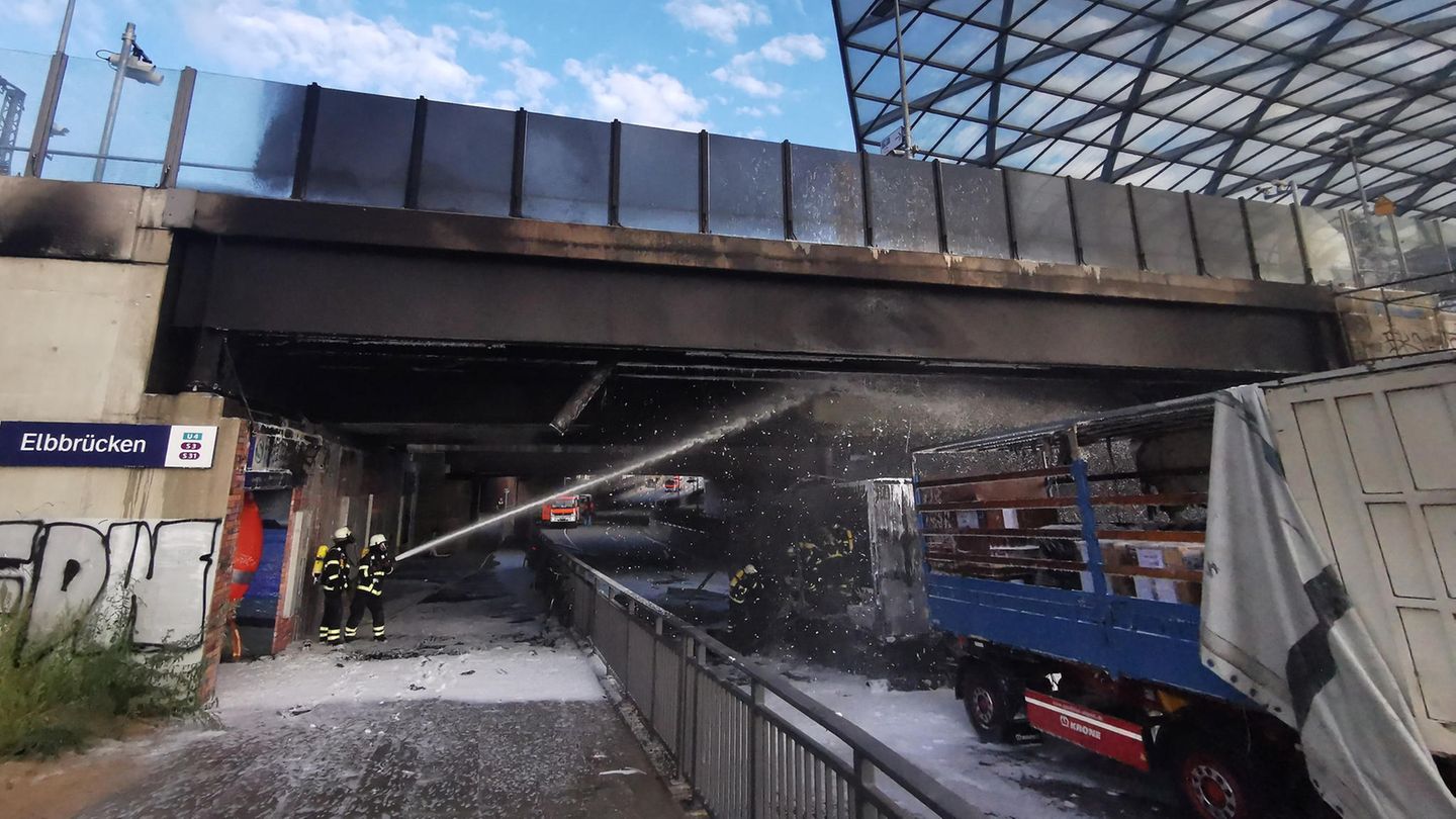 Hamburg: Zwei Feuerwehrleute löschen einen brennenden LKW, der unter einer Brücke steht