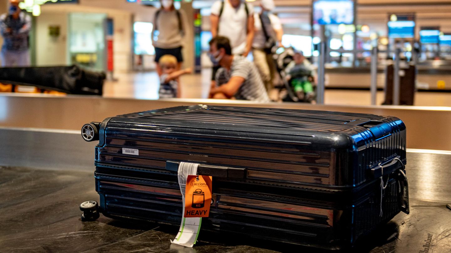 Gepäckabfertigung bei Qantas: Ein schwarzer Koffer liegt auf einem Gepäckband auf einem Flughafen, im Hintergrund Menschen