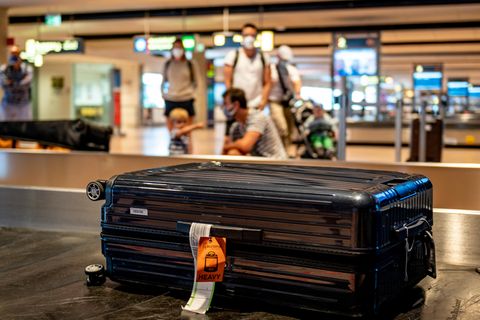 Gepäckabfertigung bei Qantas: Ein schwarzer Koffer liegt auf einem Gepäckband auf einem Flughafen, im Hintergrund Menschen