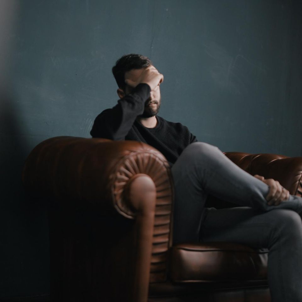 Ein Mann sitzt auf einem Ledersessel und hält sich eine Hand vors Gesicht.