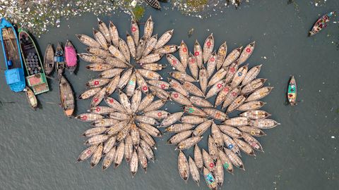 Dhaka, Bangladesch. Hunderte Holzboote warten im Hafen von Dhaka. Die bunt geschmückten Nussschalen dienen dazu, täglich Arbeiter aus den Außenbezirken der Stadt ins Zentrum zu fahren. Der Buriganga-Fluss wird jeden Tag von Millionen von Arbeitern als Weg in die Stadt Dhaka genutzt. Und während sie arbeiten, bilden die kleinen Boote aus der Luftperspektive hölzerne Blumen am Ufer.