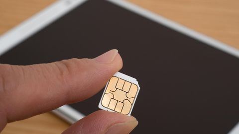 Tablet mit SIM-Karte: Eine SIM wird vor einem Tablet von einer Hand gehalten.