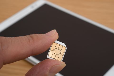 Tablet mit SIM-Karte: Eine SIM wird vor einem Tablet von einer Hand gehalten.