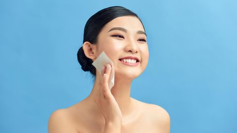Eine asiatische Frau tupft sich das Gesicht mit Blotting Paper ab