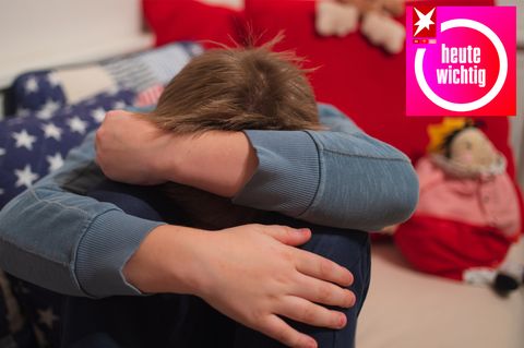 Ein Junge im Grundschulalter sitzt auf einem Bett und legt schützende die Arme um seinen Kopf