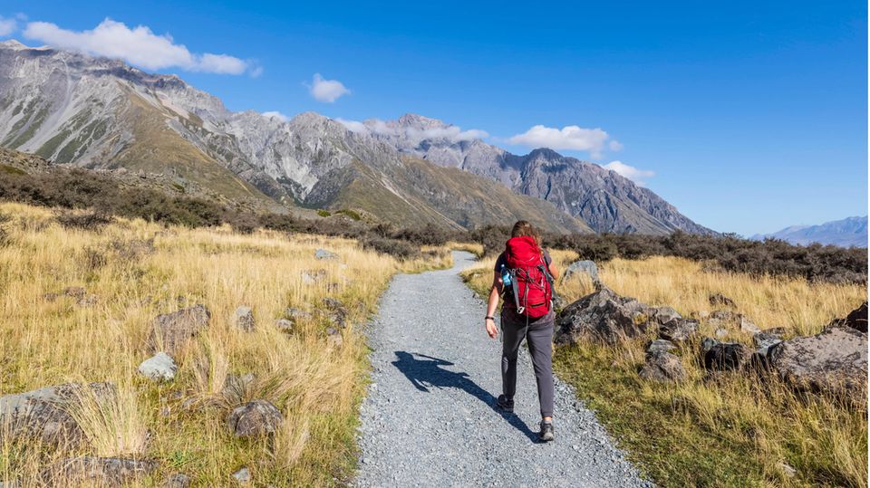Mann mit Rucksack läuft durch Landschaft in Neuseeland