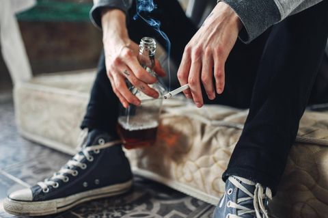 Mann hält eine Zigarette in der einen und eine Flasche Alkohol in der anderen Hand