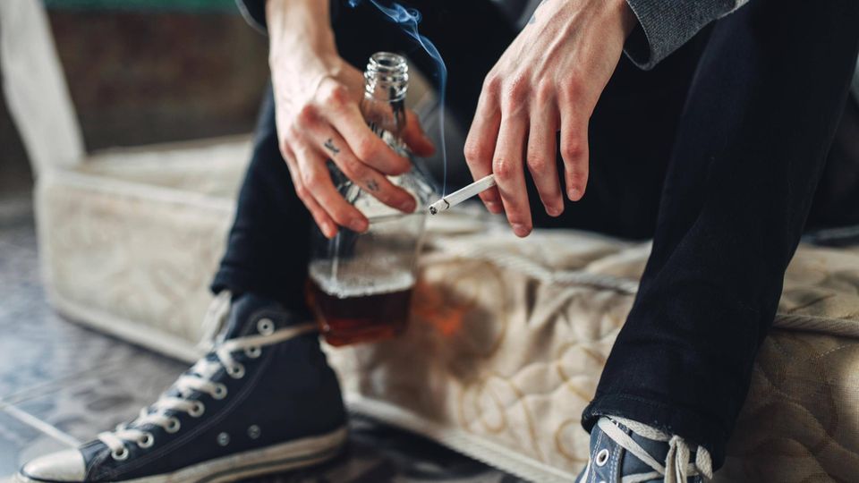 Mann hält eine Zigarette in der einen und eine Flasche Alkohol in der anderen Hand