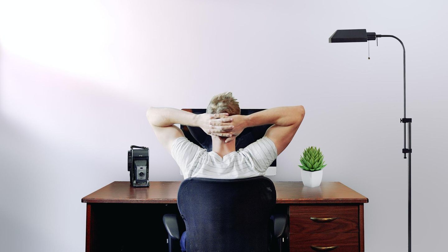 Ein Mann sitzt mit verschränkten Händen hinter dem Kopf am Schreibtisch.