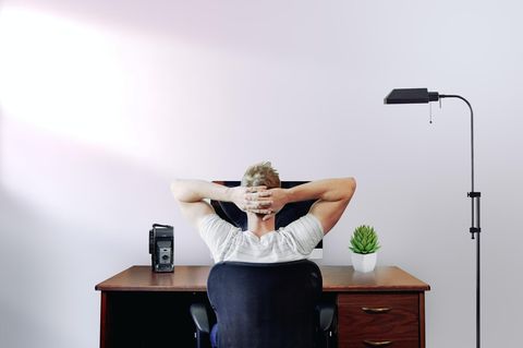 Ein Mann sitzt mit verschränkten Händen hinter dem Kopf am Schreibtisch.