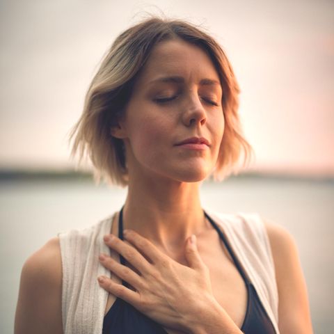 Eine Frau hält sich mit geschlossenen Augen die Hand aufs Herz.